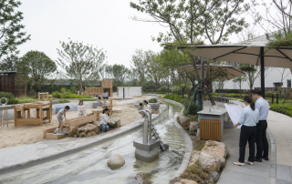 儿童在自然型沙水活动区游戏,项目人员在场地边核对系统图